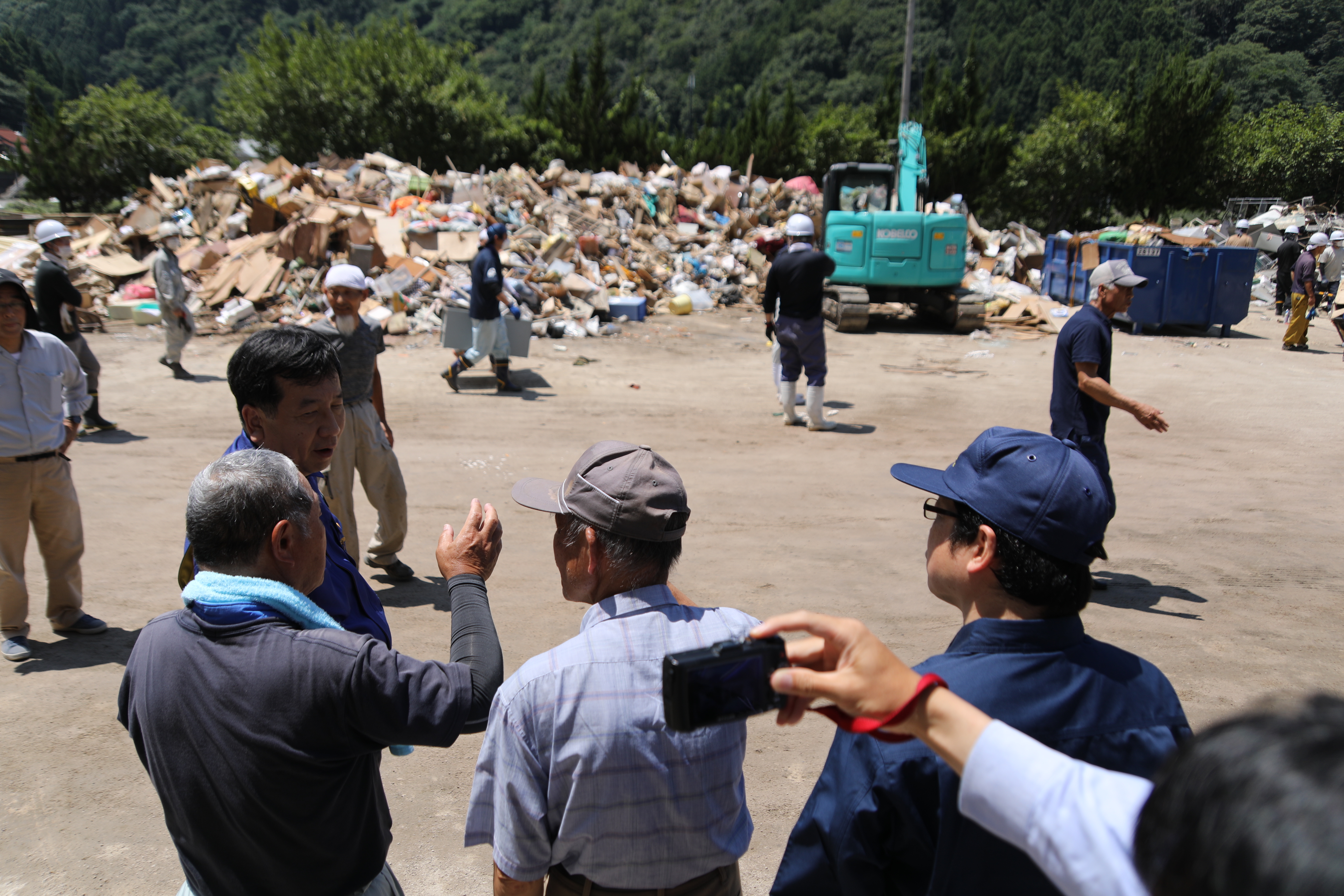 町立川越小学校跡の川越地区コミュニティ交流センターで瓦礫を前に説明を受ける枝野代表ら